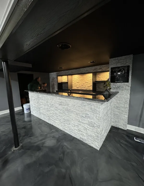 Finished basement bar with stacked-stone base and metallic epoxy floor