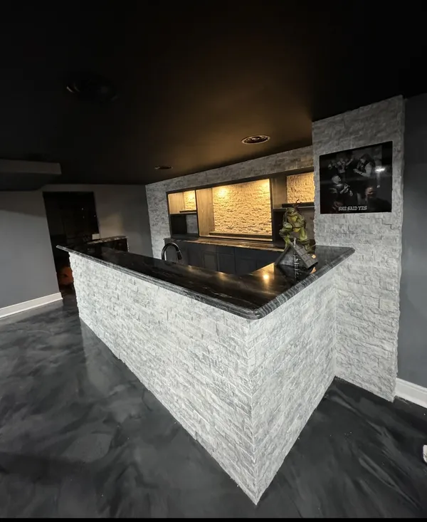Finished L-shaped basement bar with stacked-stone base and black granite top