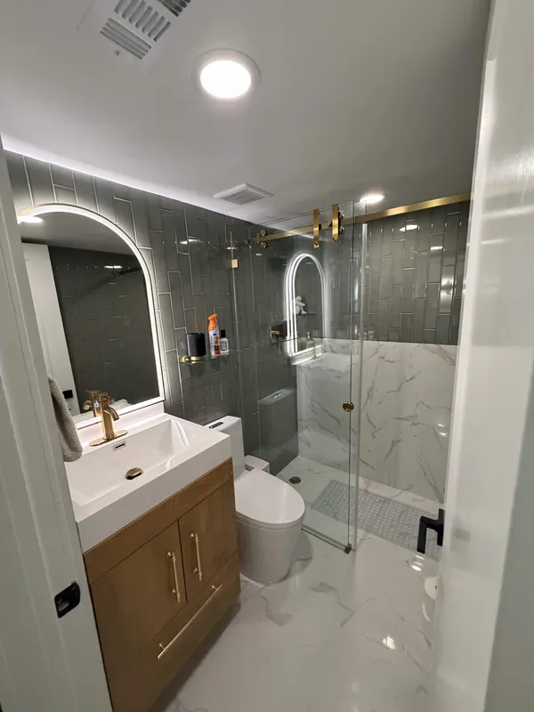 Bathroom remodel with marble walk-in shower, backlit arched mirror, and brass fixtures
