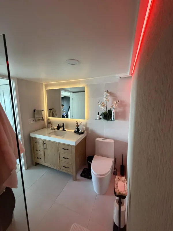Bathroom remodel with backlit vanity mirror and custom light-wood cabinetry
