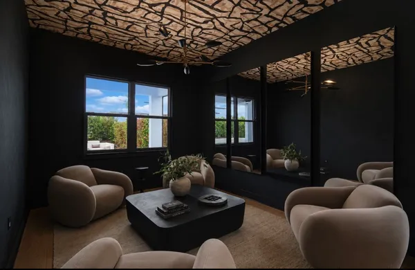 Renovated lounge with charcoal walls, mirrored accent wall, sculptural cream chairs and black wet bar